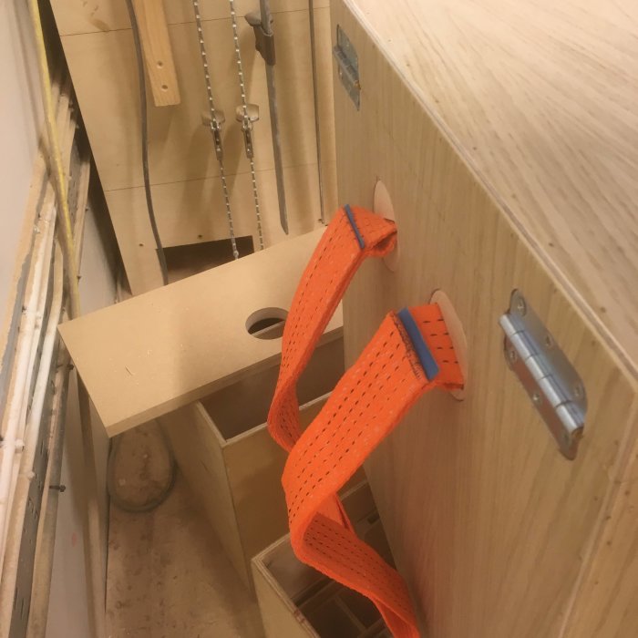 Orange spännband fastsytt till träkonstruktion i en verkstad, avsedda som bärremmar.