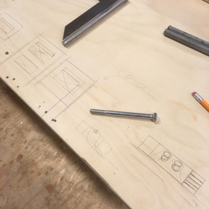 Arbetsbänk med skisser av spänndesign och remfästen, blyertspenna och skruv.