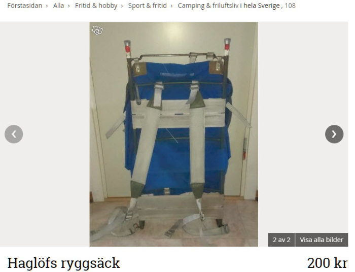 En begagnad blå Haglöfs ryggsäck med vita bärremmar och metallram, prissatt till 200 kr, visas mot vit bakgrund.
