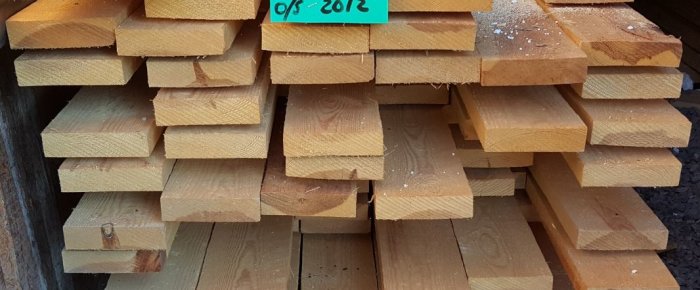 Stapel av råsågade, kvistfria furuplankor med täta årsringar lagrade utomhus.