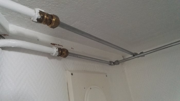 Skarvning av äldre vitmålat T-rör till stålrör och vidare till ett kopparrör mot en vit takyta.