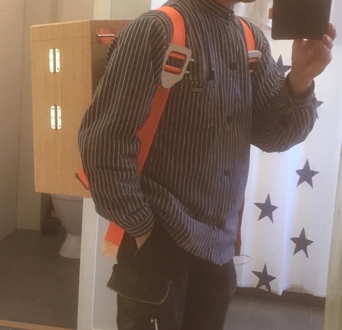Person bär träskiva på ryggen med orange spännremmar, i inomhusmiljö.