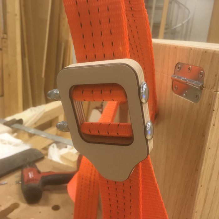Ett hemmagjort spänne av laminerad björkplywood och metallskruvar fäst på ett orange spännband.