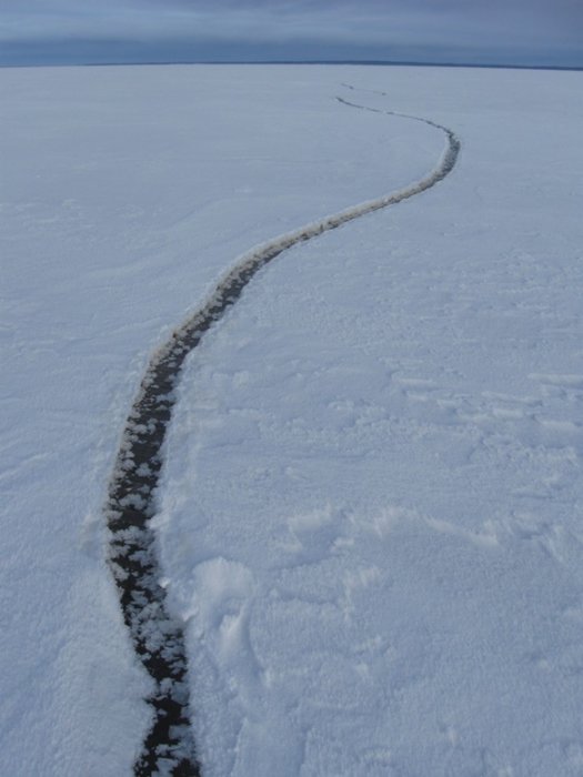 En smal råk i isen snirklar sig över ett annars helt fruset vattenlandskap.