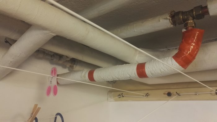 Isolerade rör i ett tak med en koppling märkt med röd tejp som indikerar änden av varmvattenledningen.