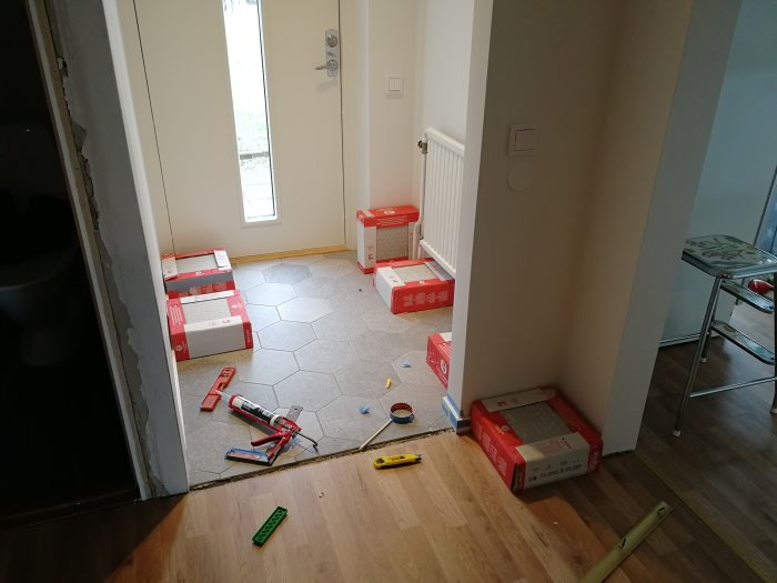 Tambur under renovering med halvlagt klinkergolv, verktyg och klinkerförpackningar använts som vikter.