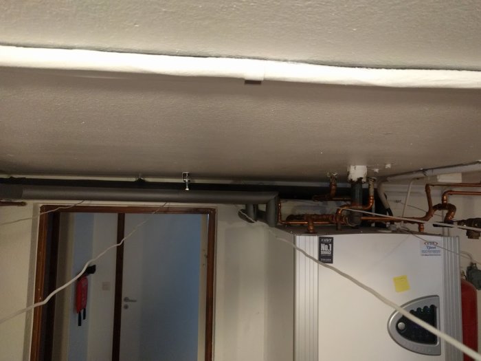 Rördragning längs med taket ovanför en vattenberedare i ett teknikrum.