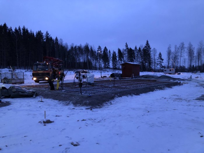 Betongbil och arbetare förbereder gjutning av grund i vinterlandskap vid gryning.