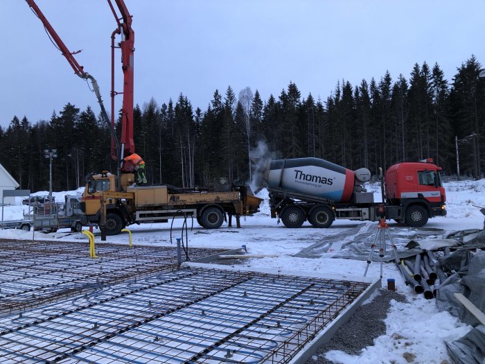 Gjutning av betongplatta i vintermiljö med betongbil och kranbil på byggarbetsplats.