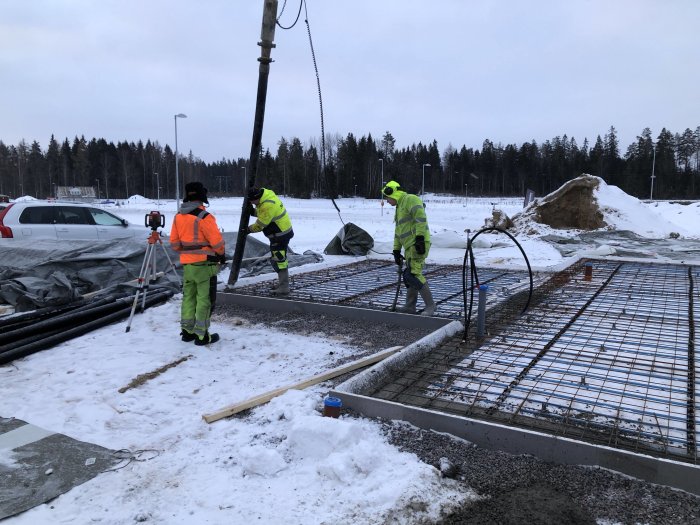 Arbetsplats med arbetare som förbereder för betonggjutning i kallt väder med synliga armeringsjärn och byggmaterial.