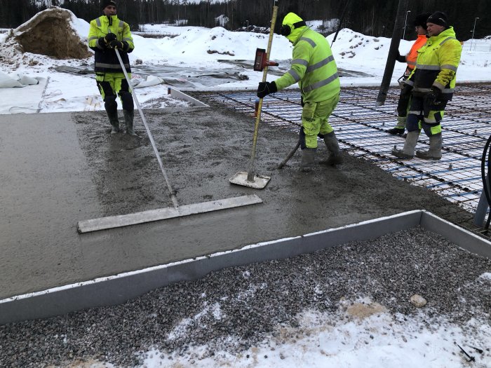 Arbetare jämnar ut nyligen gjuten betong på en byggplats i kallt väder.