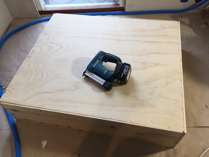 En verktygslåda av plywood med en elektrisk häftpistol ovanpå i ett under konstruktion rum.