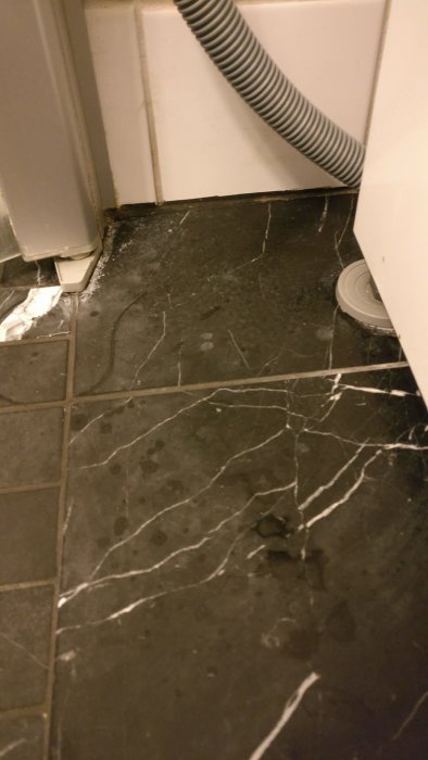 Mörkt marmorgolv med missfärgningar och sträv yta efter användning av rengöringsmedel, med skadat område uppe till höger.