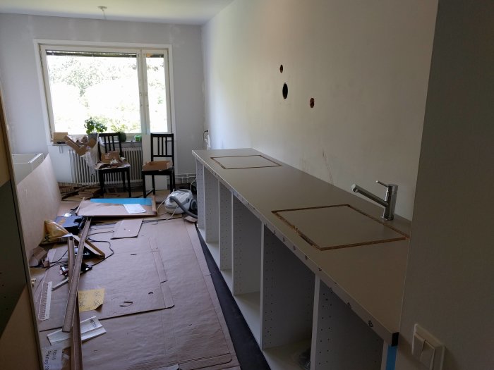 Kök under renovering med nya osammanbyggda skåpstommar och tillfälligt placerad bänkskiva och kran.