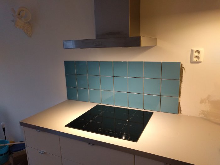 Nytt kök med vit bänkskiva, blå kakelplattor, induktionshäll och rostfri köksfläkt, pågående renovering.