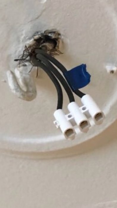 Öppen elektrisk dosa med svarta kablar och vita kopplingsklämmor mot en vit vägg.