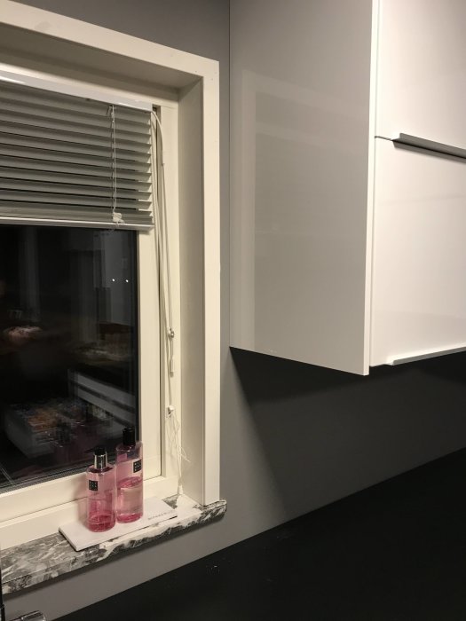 Köksfönster med smalare fodral, persienner och en delvis installerad stänkpanel vid bänkskivan.