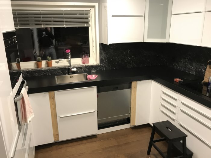 Kök under renovering med vit inredning, svart bänkskiva och ej färdigställda skåp och lister.