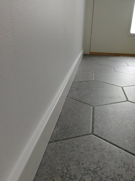 Nyligen listad tambur med vitmålad fotlist längs en gråmålad vägg ovanför gråa kakelplattor.