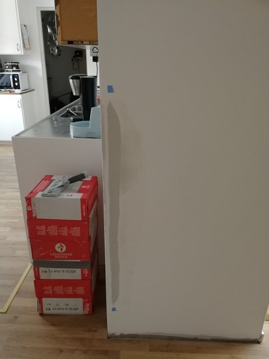 Vägg i hemmiljö med nyligen installerad list och synlig fog, spacklad skarv synlig, kartonger på golvet.
