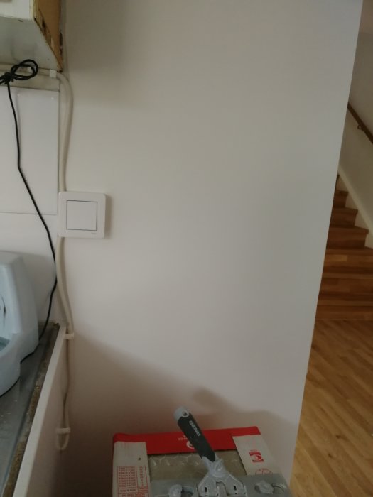 Färdiglistad tambur med nyligen installerad brytare och spacklad vägg, oavslutat installationstillbehör syns.