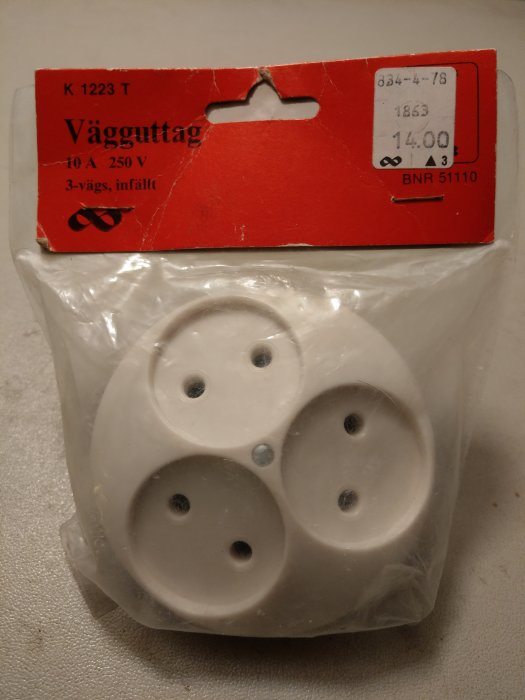 Oöppnad förpackning med gammalt klassiskt trefacks vägguttag i vitt.