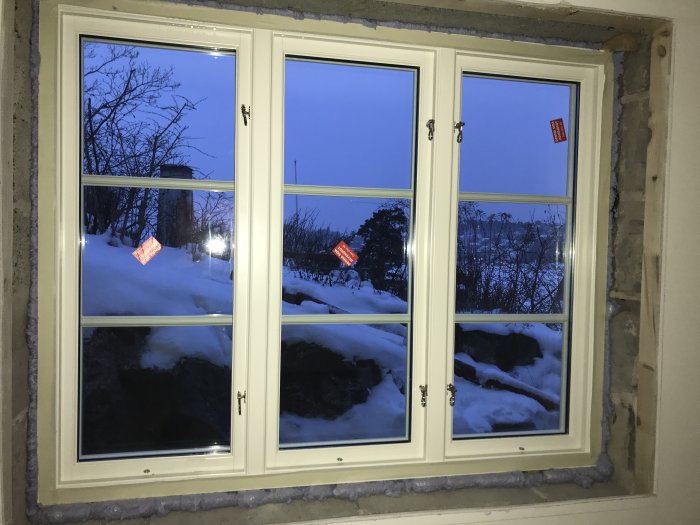 RM fönster installerade i en vägg, synliga spröjs endast på utsidan med snöig natur utanför i skymningen.