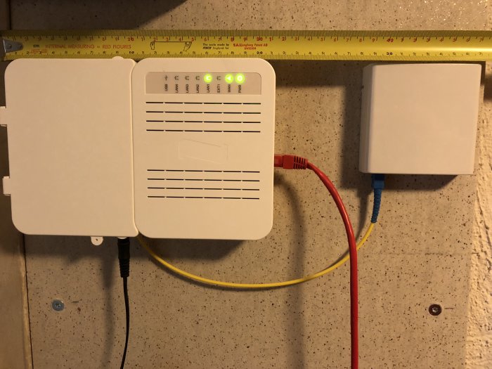 Fiberanslutningsboxar på källarvägg med inkommande fiberkabel och nätverkskablar.