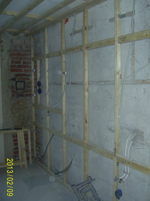 En orenoverad vägg med reglar och fördragna elektriska rör i ett pågående byggprojekt.