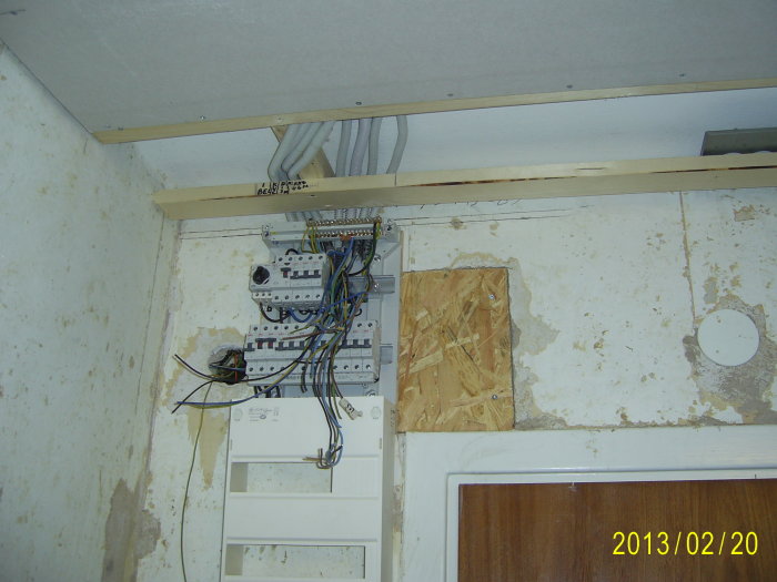 Elcentral med öppna kablar och fördragna rör installerade ovanför en dörr.