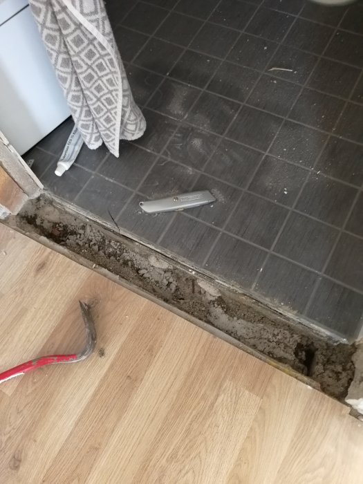 Ett golv med delvis upptagen betongtröskel och verktyg, vilket visar en arbetsdel i en renoveringsprocess.