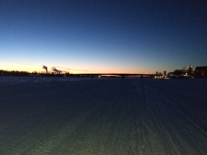 Vinterkvällsbild av Kalixbron med svag solnedgång i bakgrunden och snötäckt mark i förgrunden.