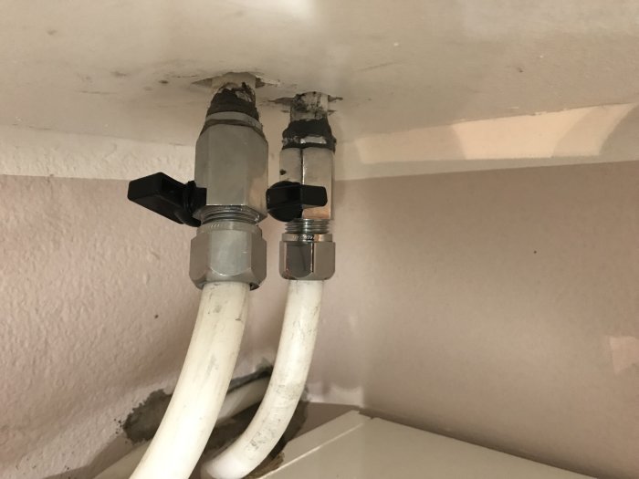 Två nyinstallerade rörkopplingar med vred på en vägg, installationsområdet ser ojämnt och potentiellt snett ut.