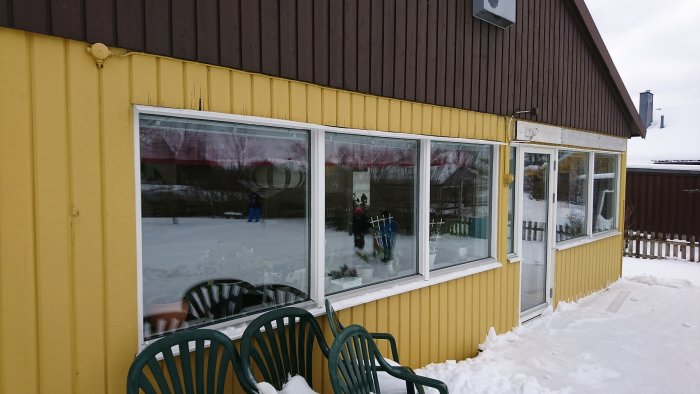 Del av hus med fönster och sliten träpanel ovanför samt några plankor på sidan med synliga skador.