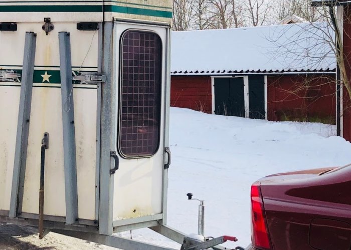 Hästtransport framvägg med tecken på slitage nära marken, står i snöigt landskap.