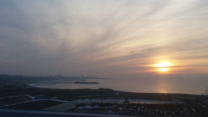 Vy över Malmö med solnedgång över havet och silhuetten av byggnader i horisonten.