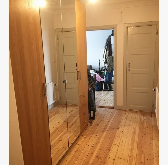 Nyinstallerad garderob med spegeldörrar i ett sovrum med trägolv och vita dörrar i bakgrunden.
