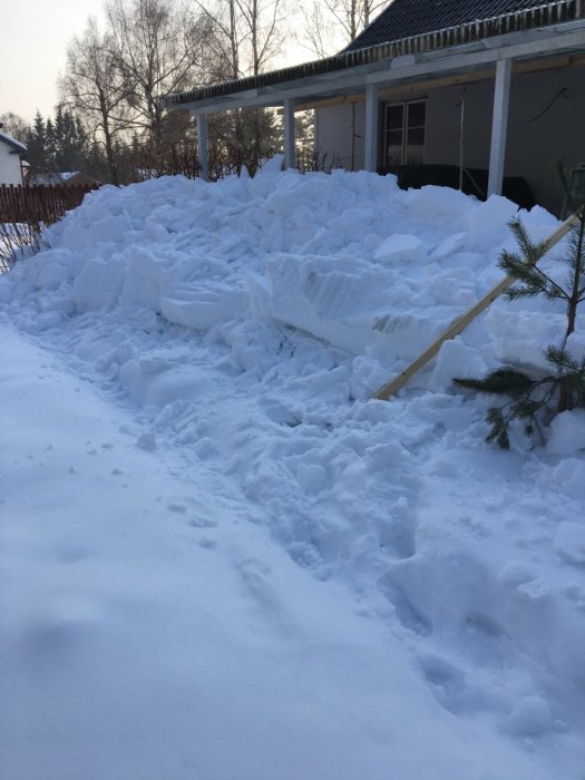 En stor hög av nyskottad snö framför ett hus med en veranda täckt av snö.