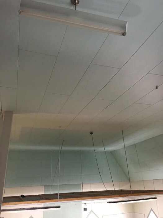 Sloped white inner ceiling with three ventilation grilles and a fluorescent light fixture in a building.