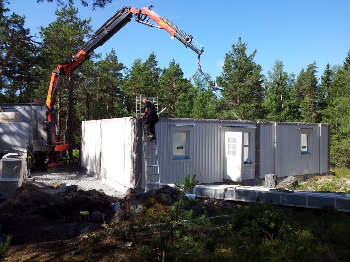 Stomresning av ett hus med en kranbil som lyfter en sektion, medan en person arbetar på en stege.