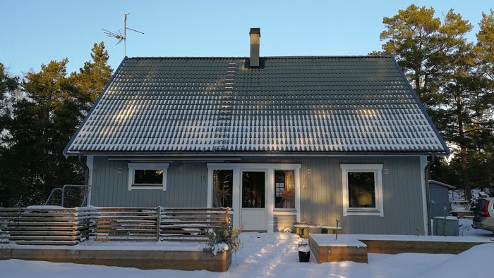 Nyligen färdigbyggt grått hus i snölandskap med solnedgång på vintern.