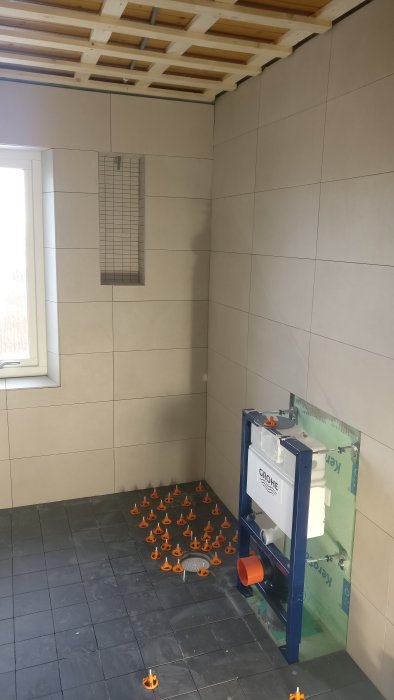 Delvis färdigbyggt badrum med kaklade väggar, installationsram för toalett och golvfästen.