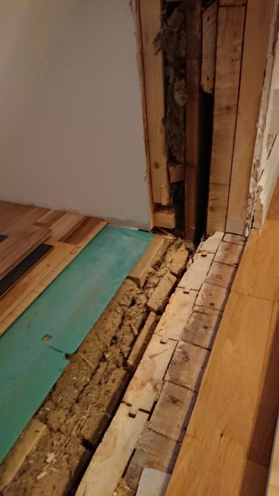 Delvis öppnad vägg och golv i en renoveringsfas visar skillnad i golvhöjd och isoleringsmaterial mellan rummen.
