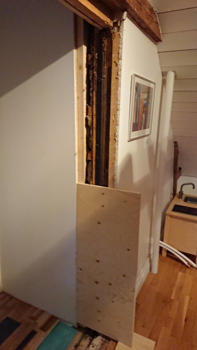 En öppning i väggen med synliga reglar och plywoodskiva, skillnad i golvhöjder syns.