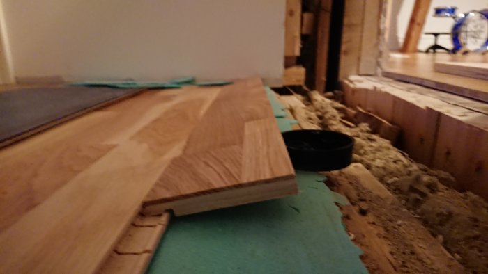 Närbild av golvnivåskillnad vid byggprojekt med plywood och träbjälkar.