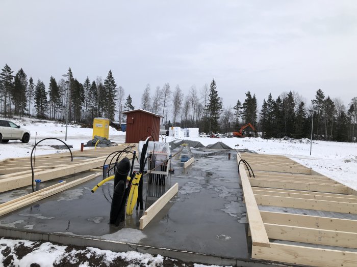 Nybyggd stomme till ett garage på en grå betongplatta med byggmaterial och snö i bakgrunden.