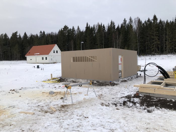 Stomme till ett nybyggt garage med gipsade väggar på en vinterbyggarbetsplats, med hus i bakgrunden.