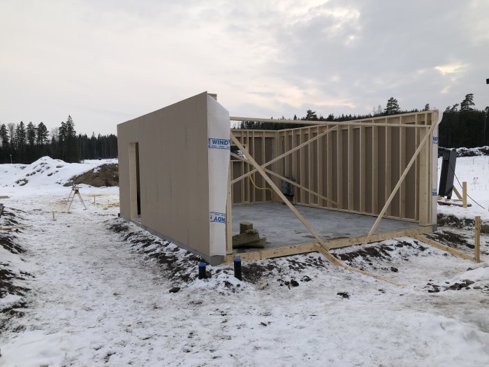 Byggstommen till ett garage med gipstäckta väggar på en byggplats med snötäckt mark.