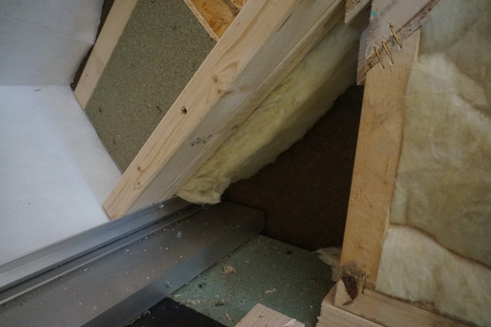 Vinkelvy av vind med exponerad isolering och synlig aluminiumprofil i anslutning till träkonstruktion.