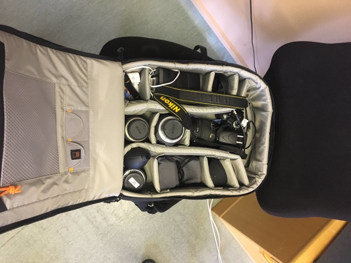 Öppen kameraväska med Nikon 5100 systemkamera och olika objektiv samt tillbehör ordnade inne i fack.